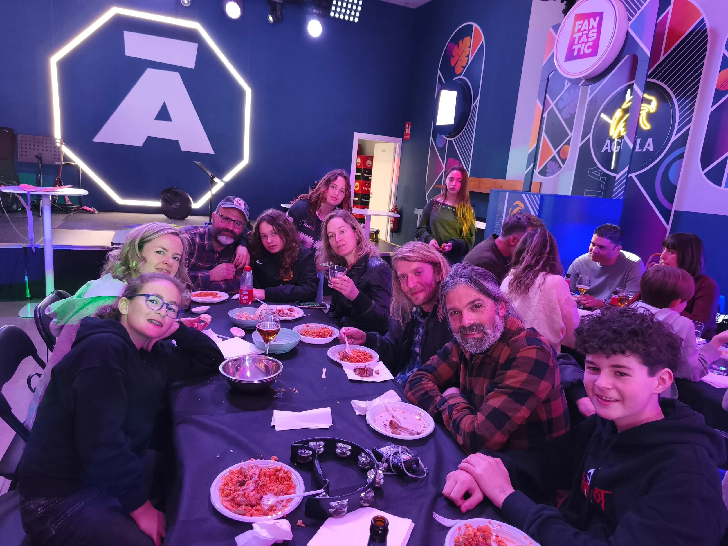Miembros de la comunidad Turia Rock Club, familias y músicos, comiendo juntos en una mesa larga tras un evento